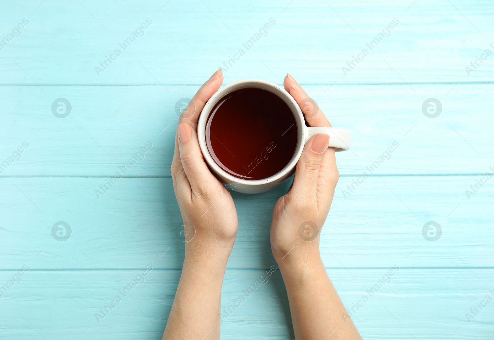 Photo of Woman with cup of tea at light blue wooden table, top view