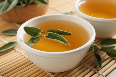 Photo of Cup of aromatic sage tea with fresh leaves on table, closeup