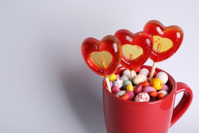 Photo of Delicious heart shaped lollipops and dragees on light background