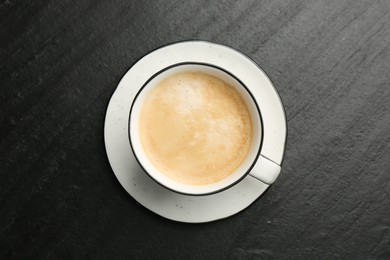 Photo of Tasty cappuccino in cup and saucer on dark textured table, top view