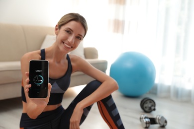 Young woman showing smartphone with fitness app indoors, focus on device