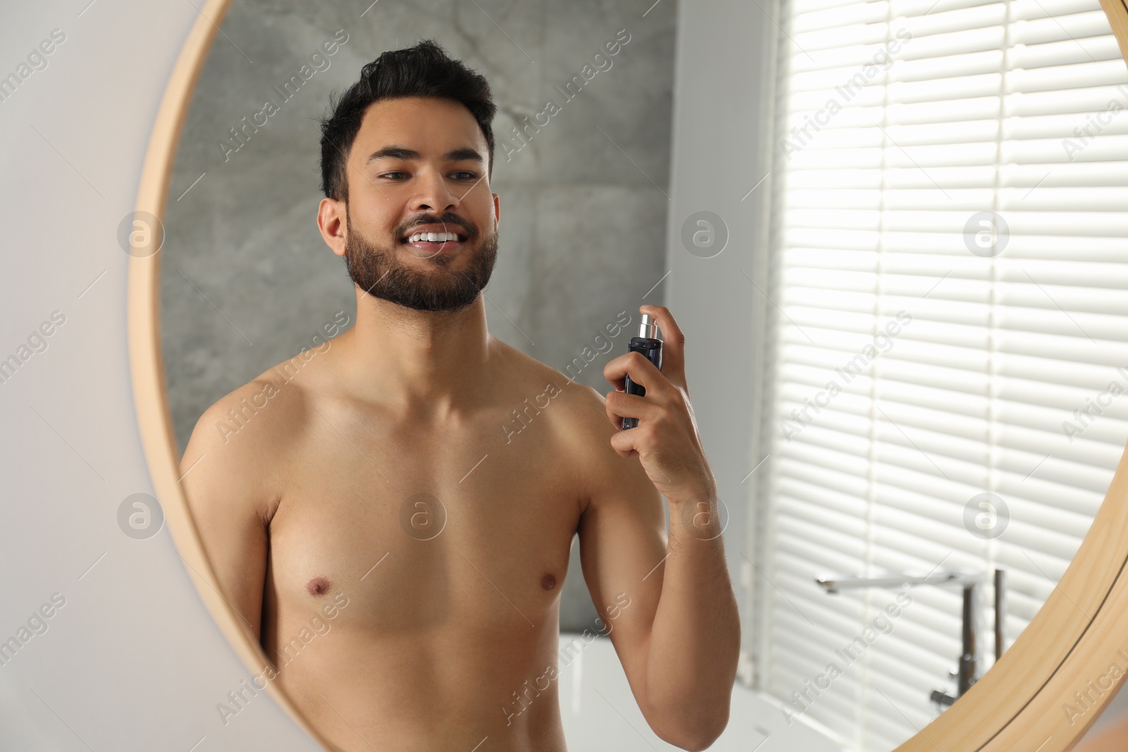 Photo of Man spraying luxury perfume near mirror indoors