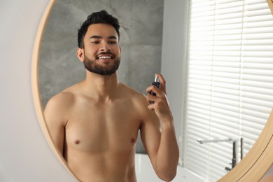 Man spraying luxury perfume near mirror indoors