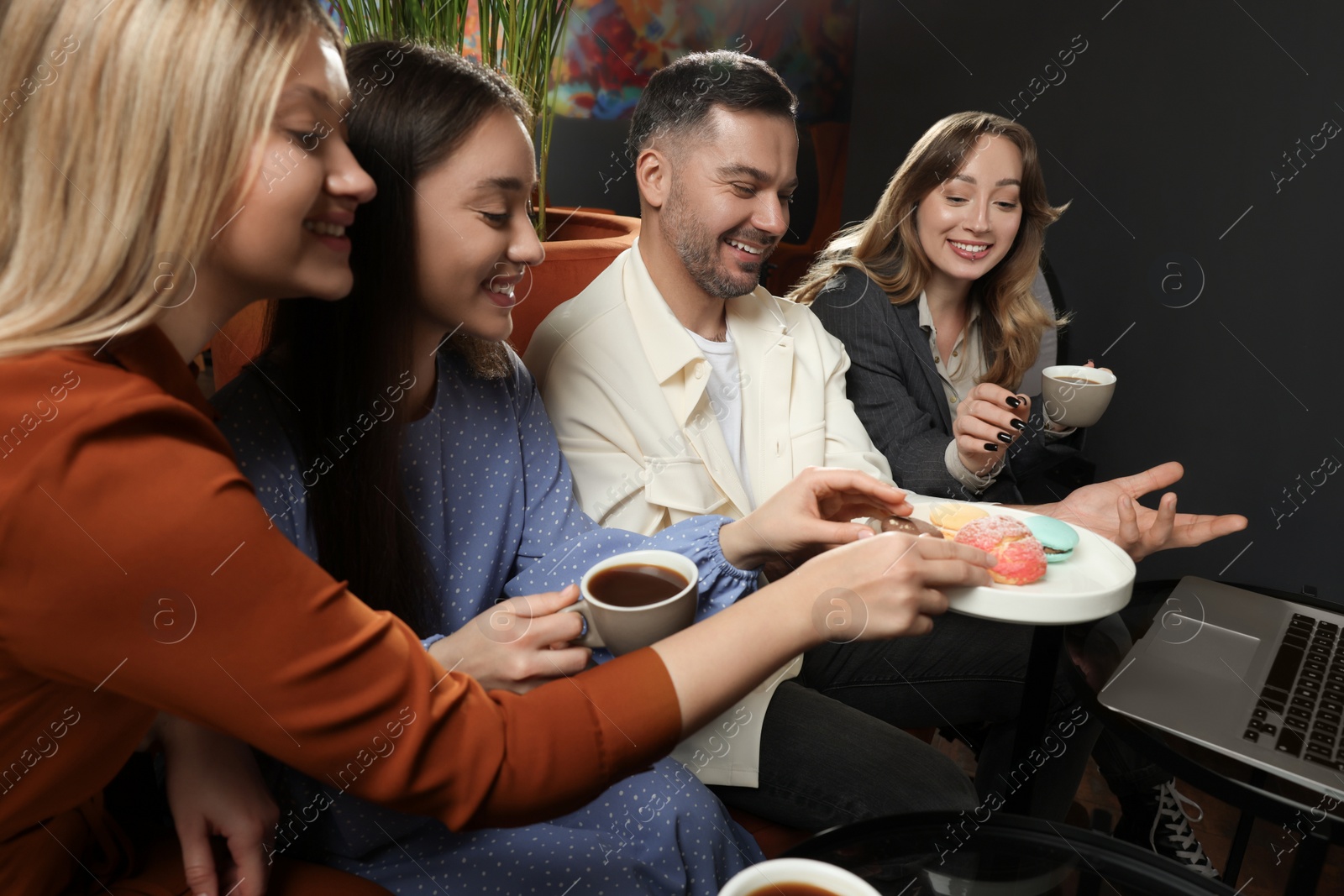 Photo of People with coffee, macarons and laptop spending time together in cafe