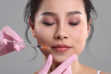 Photo of Woman getting lip injection on grey background, closeup