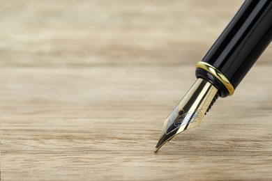 Photo of Stylish fountain pen on wooden table, closeup. Space for text