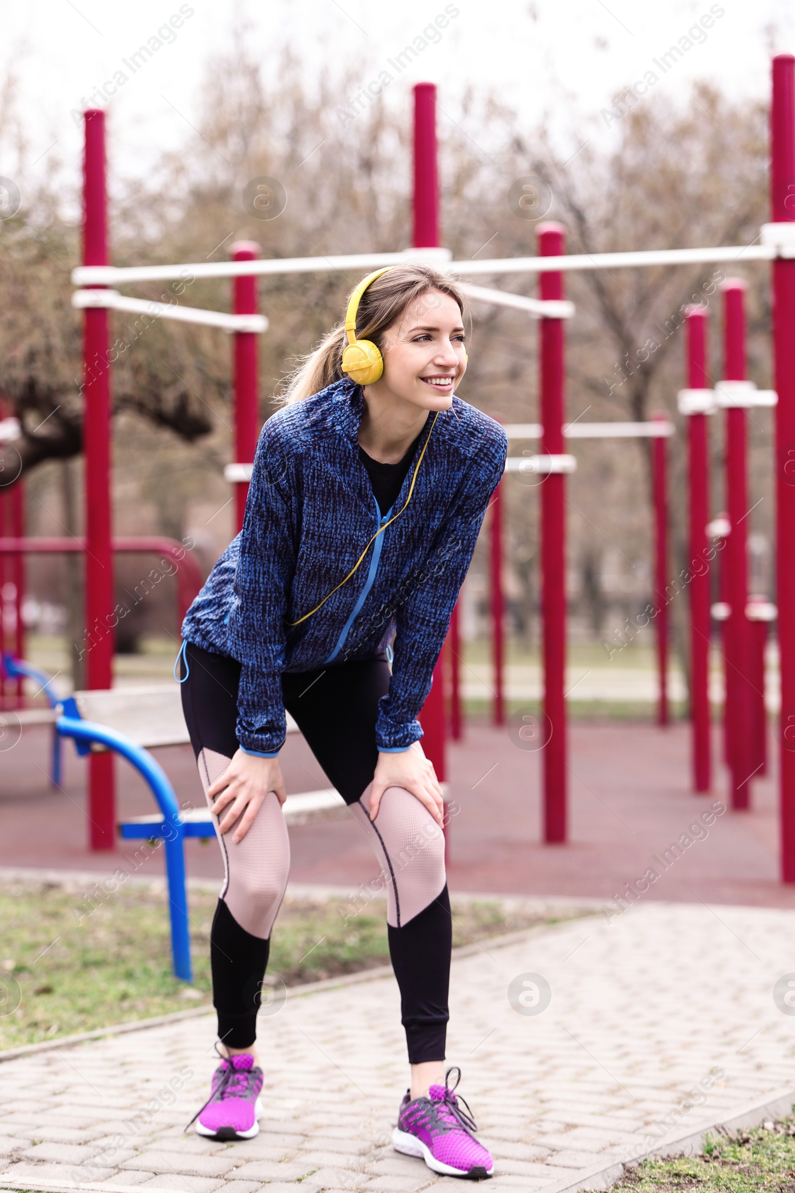 Photo of Young woman with headphones listening to music and exercising on sports ground
