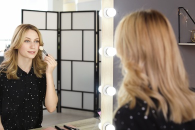 Young woman applying makeup near mirror in dressing room