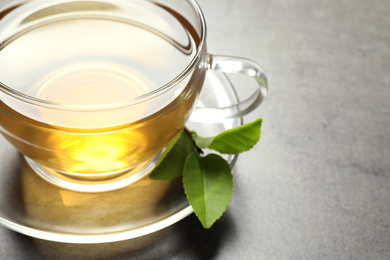 Cup of green tea and leaves on grey table, closeup. Space for text