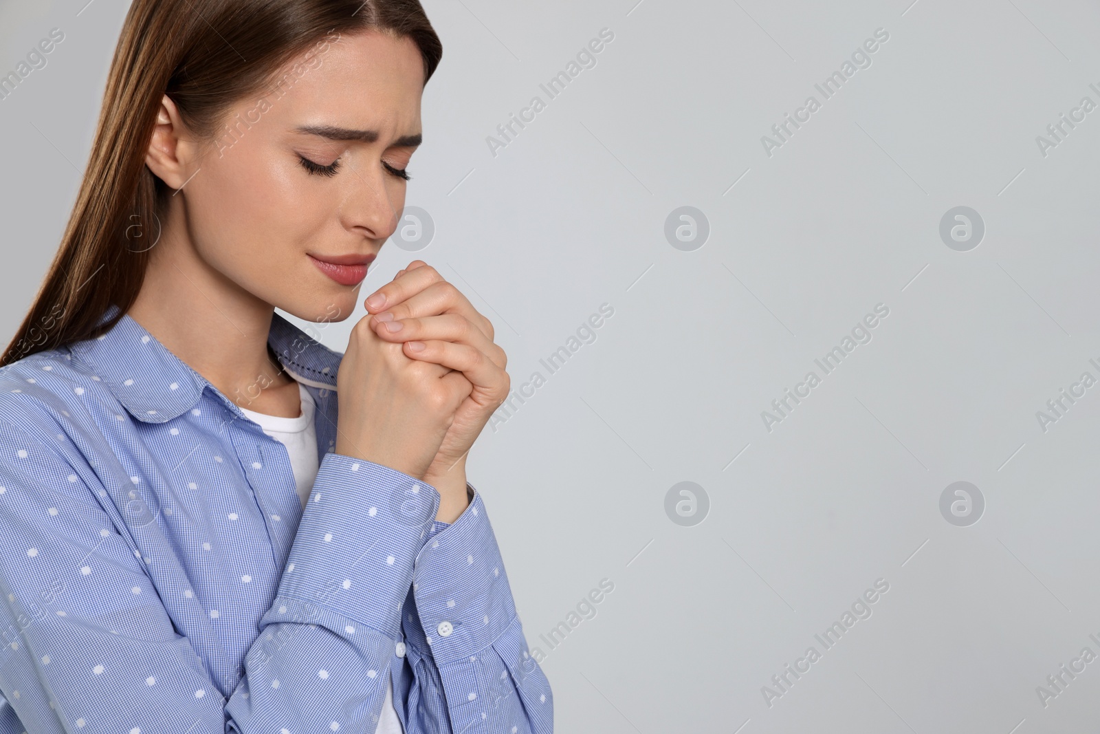 Photo of Woman with clasped hands praying on light grey background, space for text