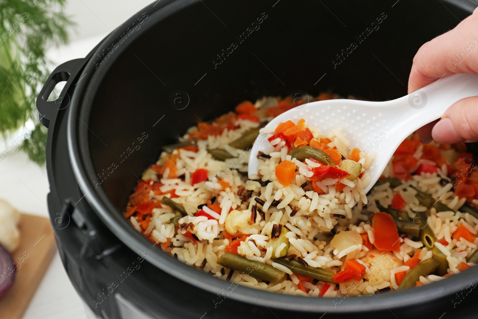 Photo of Woman preparing rice with vegetables in multi cooker, closeup