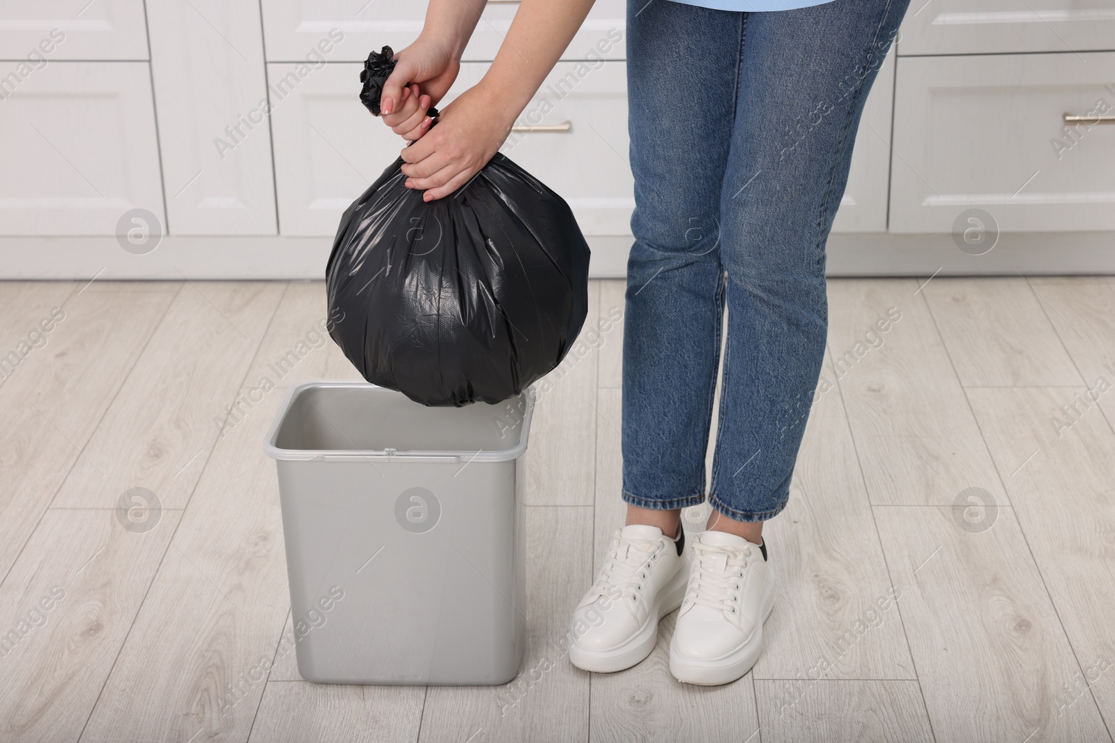 Photo of Woman taking garbage bag out of trash bin in kitchen, closeup