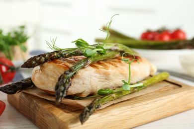 Tasty grilled chicken fillet served with asparagus and sprouts on wooden board, closeup