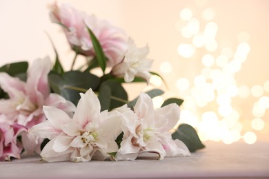 Photo of Bouquet of beautiful lily flowers on table against beige background with blurred lights, closeup. Space for text