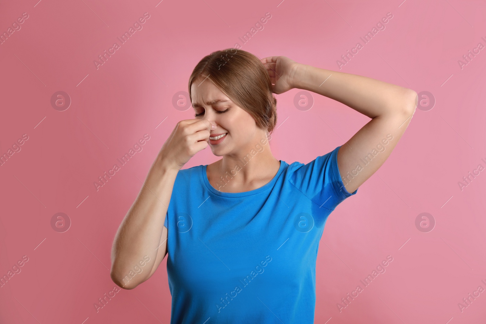 Photo of Young woman with sweat stain on her clothes against pink background. Using deodorant