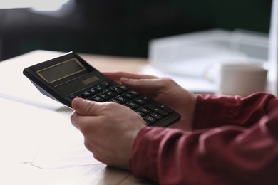 Man using calculator at wooden table indoors, closeup