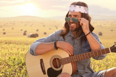 Photo of Portrait of happy hippie man with guitar in field, space for text