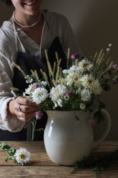 Photo of Smiling woman creating beautiful flower arrangement at wooden table, closeup
