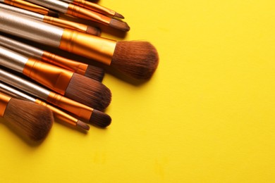 Photo of Different makeup brushes on yellow background, closeup. Space for text