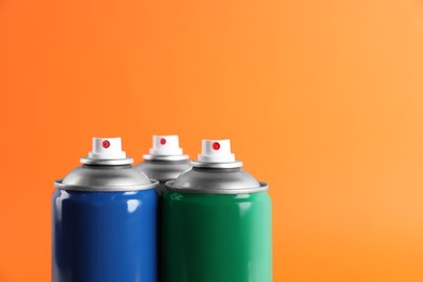 Photo of Colorful cans of spray paints on orange background, closeup. Space for text