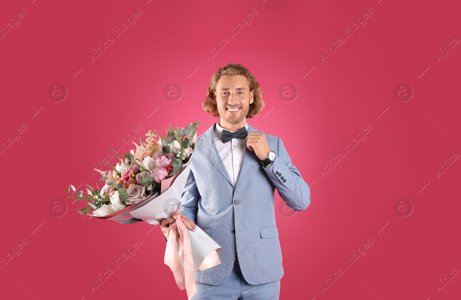 Photo of Young handsome man in stylish suit with beautiful flower bouquet on pink background