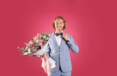 Photo of Young handsome man in stylish suit with beautiful flower bouquet on pink background