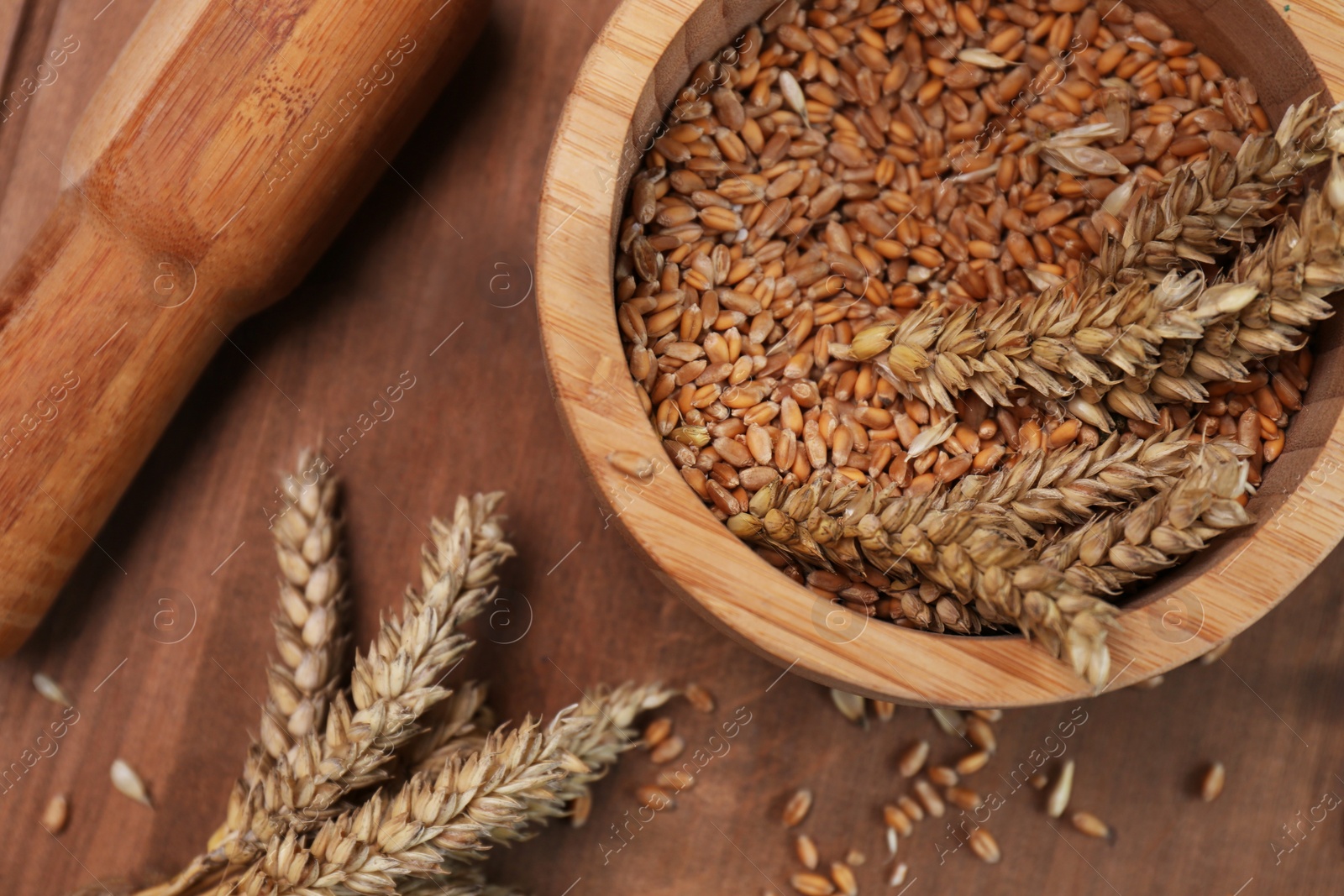 Photo of Mortar, pestle and ears of wheat on wooden table, flat lay