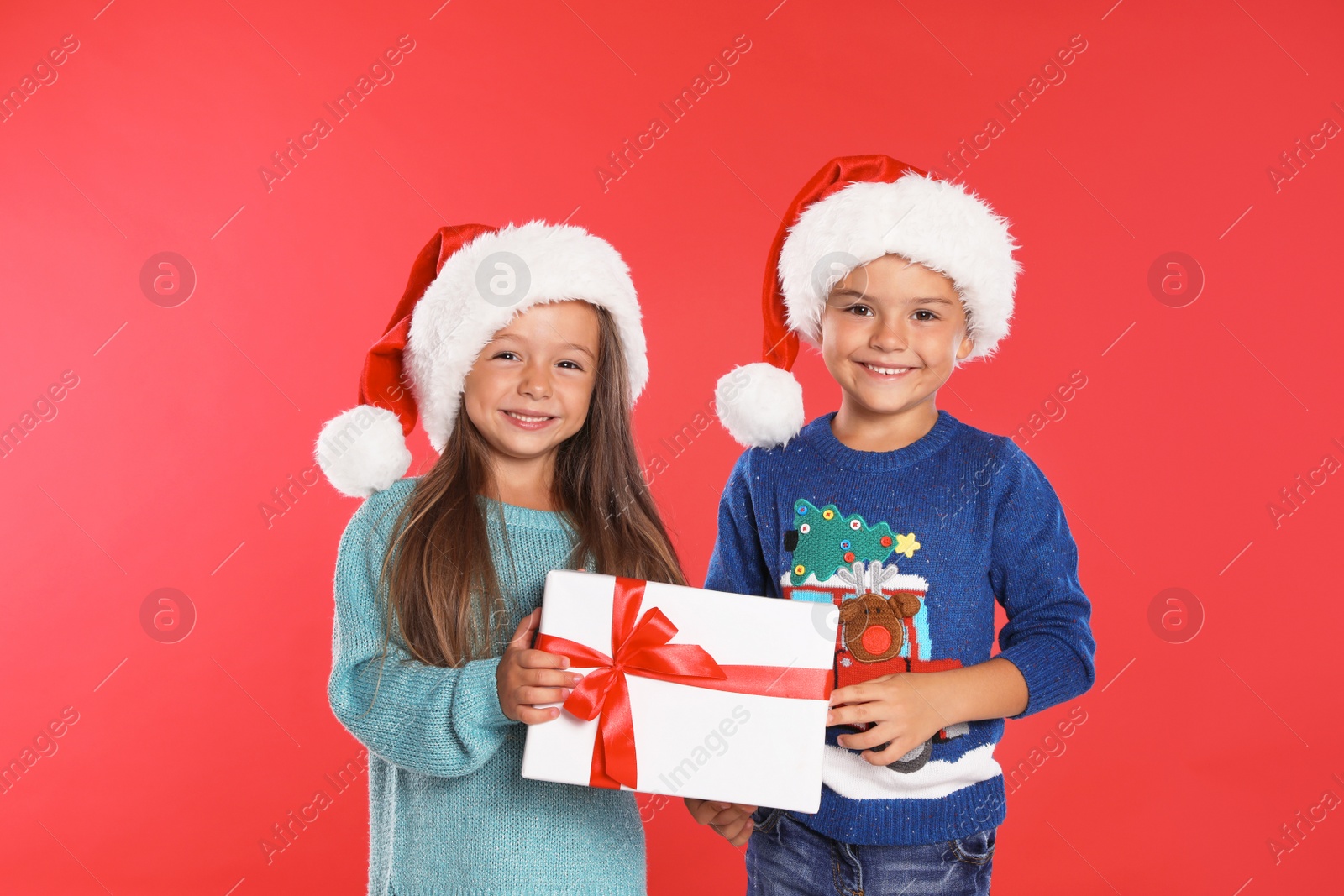 Photo of Happy little children in Santa hats with gift box on red background. Christmas celebration