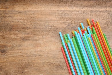Photo of Colorful plastic drinking straws on wooden table, flat lay. Space for text