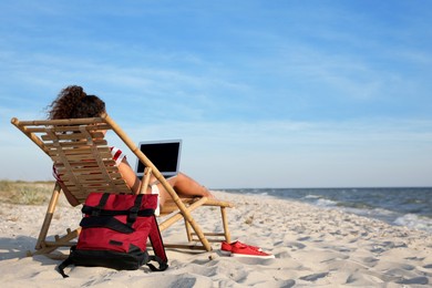 Photo of African American woman working on laptop in sunbed at beach