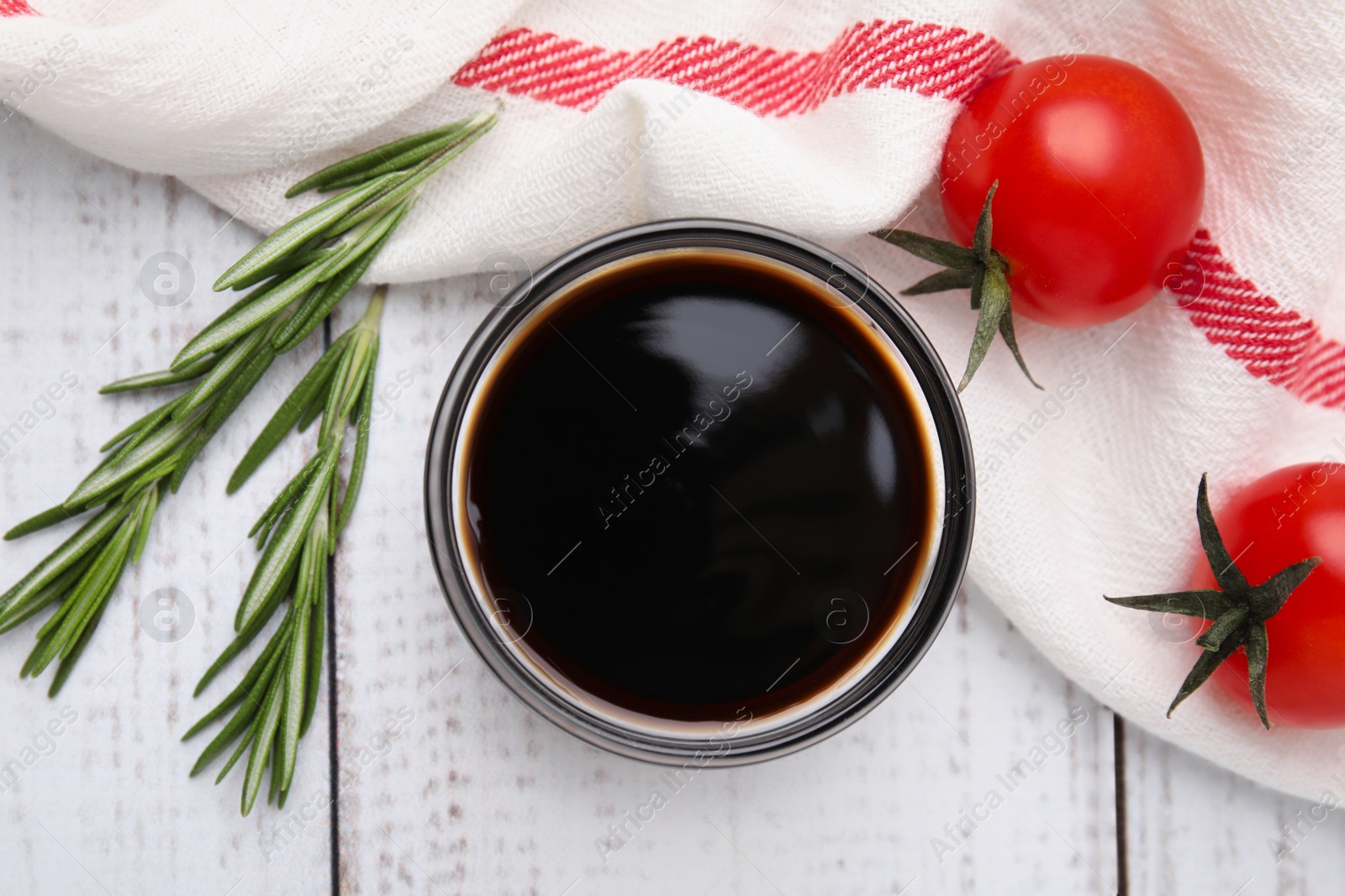 Photo of Bowl with balsamic vinegar, rosemary and tomatoes on white wooden table, flat lay