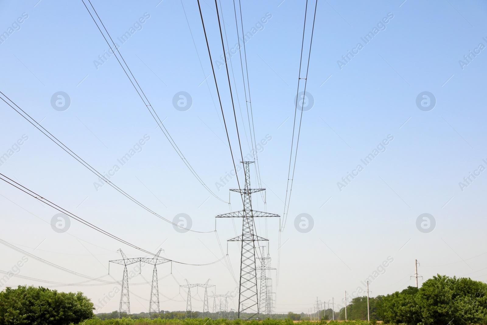 Photo of High voltage towers with electricity transmission power lines in field on sunny day