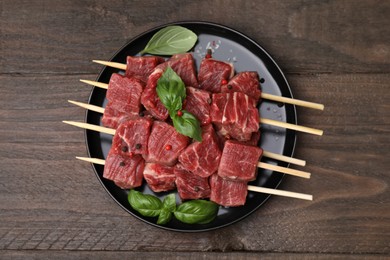 Photo of Skewers with cut fresh beef meat, basil leaves and spices on wooden table, top view