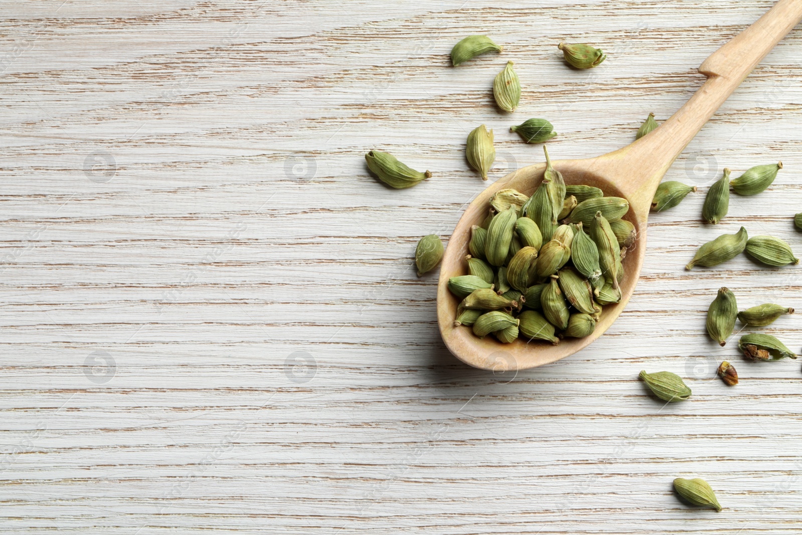 Photo of Spoon with dry cardamom pods on white wooden table, top view. Space for text