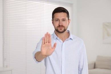 Photo of Handsome man showing stop gesture at home