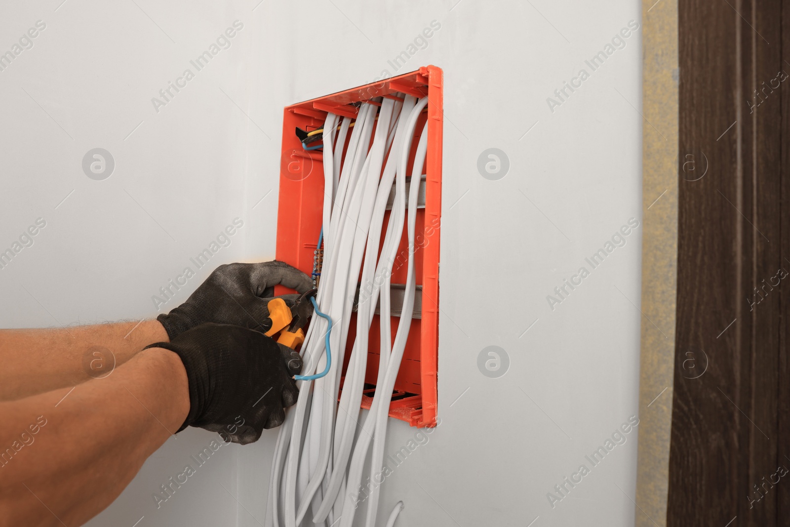 Photo of Electrician with pliers installing switchboard indoors, closeup