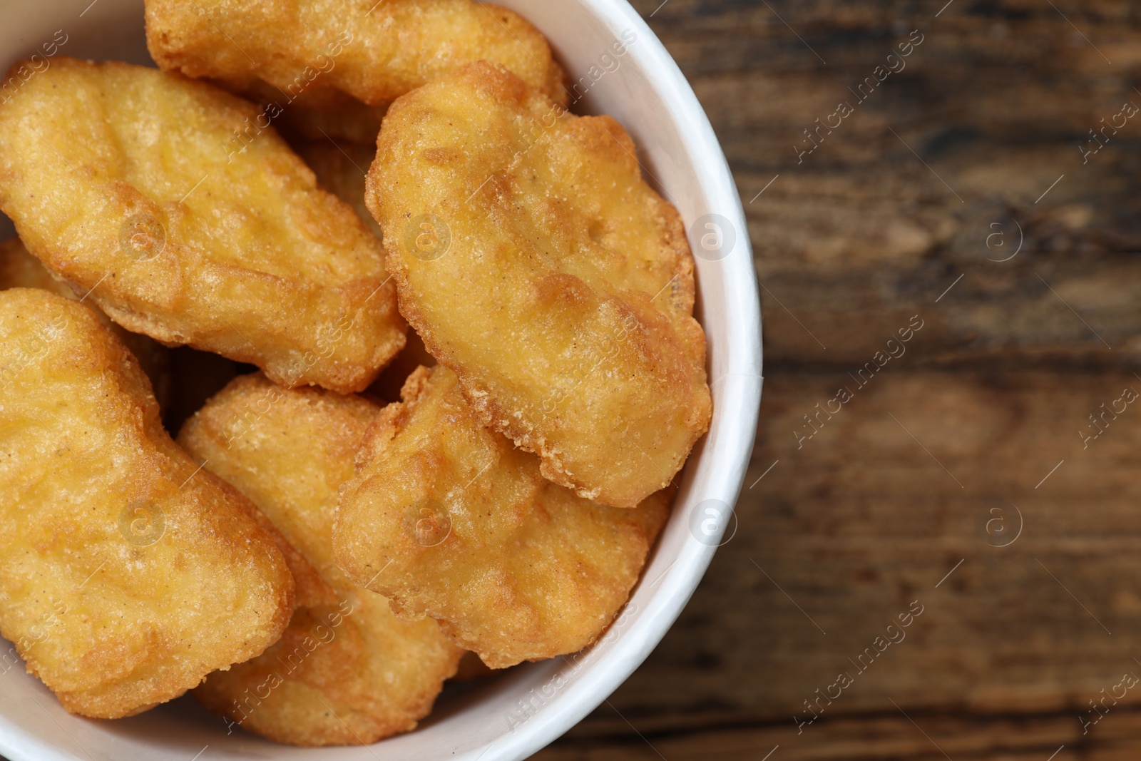 Photo of Bucket with tasty chicken nuggets on wooden table, top view