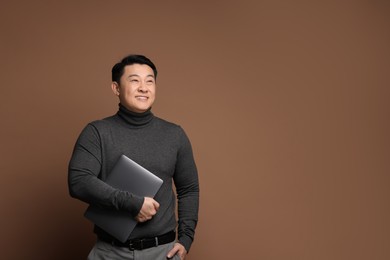 Photo of Portrait of happy man with laptop on brown background. Space for text