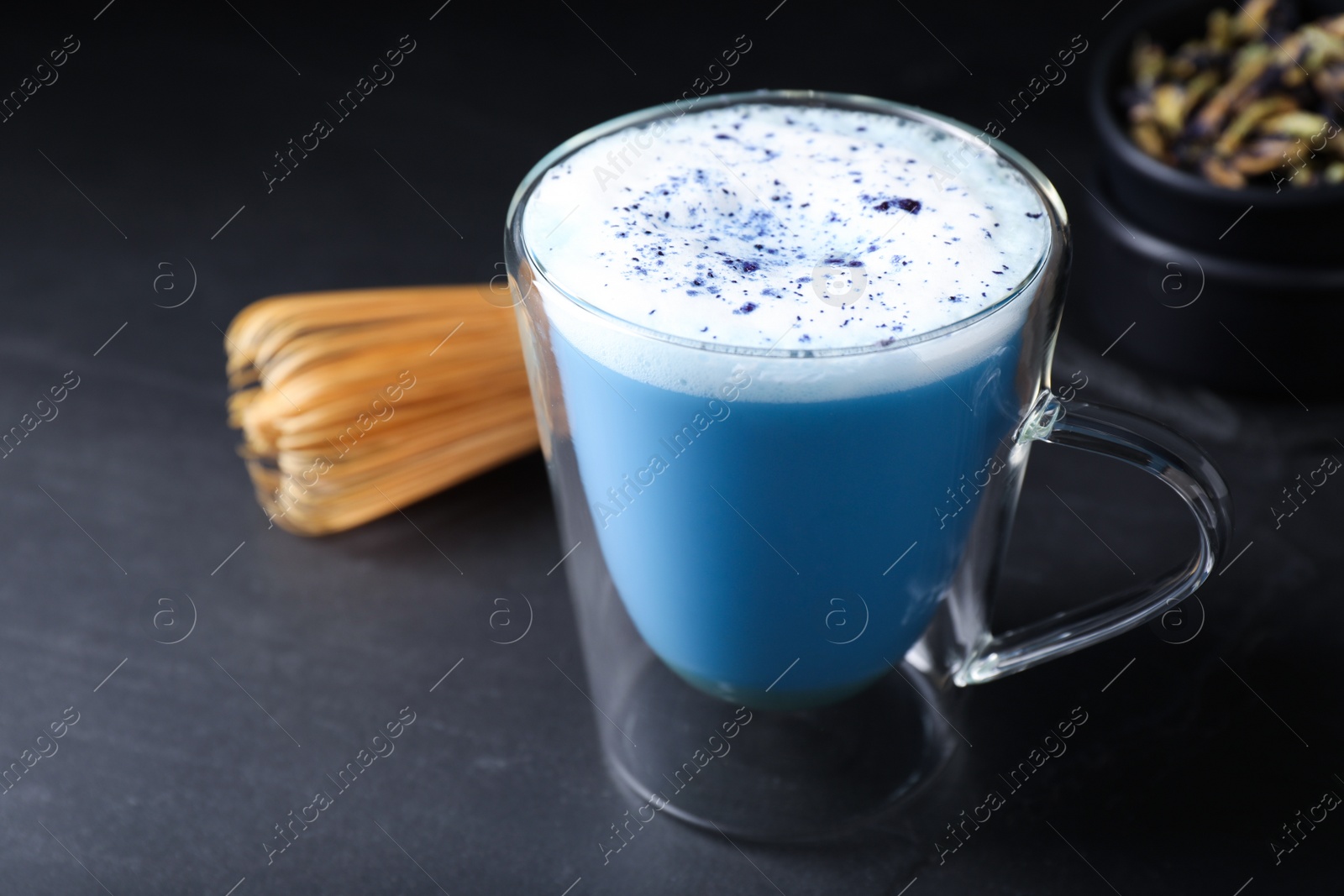 Photo of Delicious blue matcha drink and chasen on black table, closeup