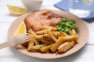 Tasty fish, chips, peas and lemon on white wooden table, closeup