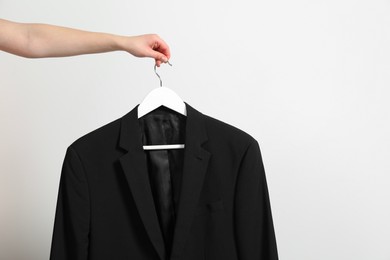 Photo of Woman holding hanger with black jacket near white wall, closeup. Space for text