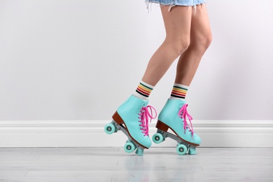 Photo of Young woman with retro roller skates near white wall, closeup