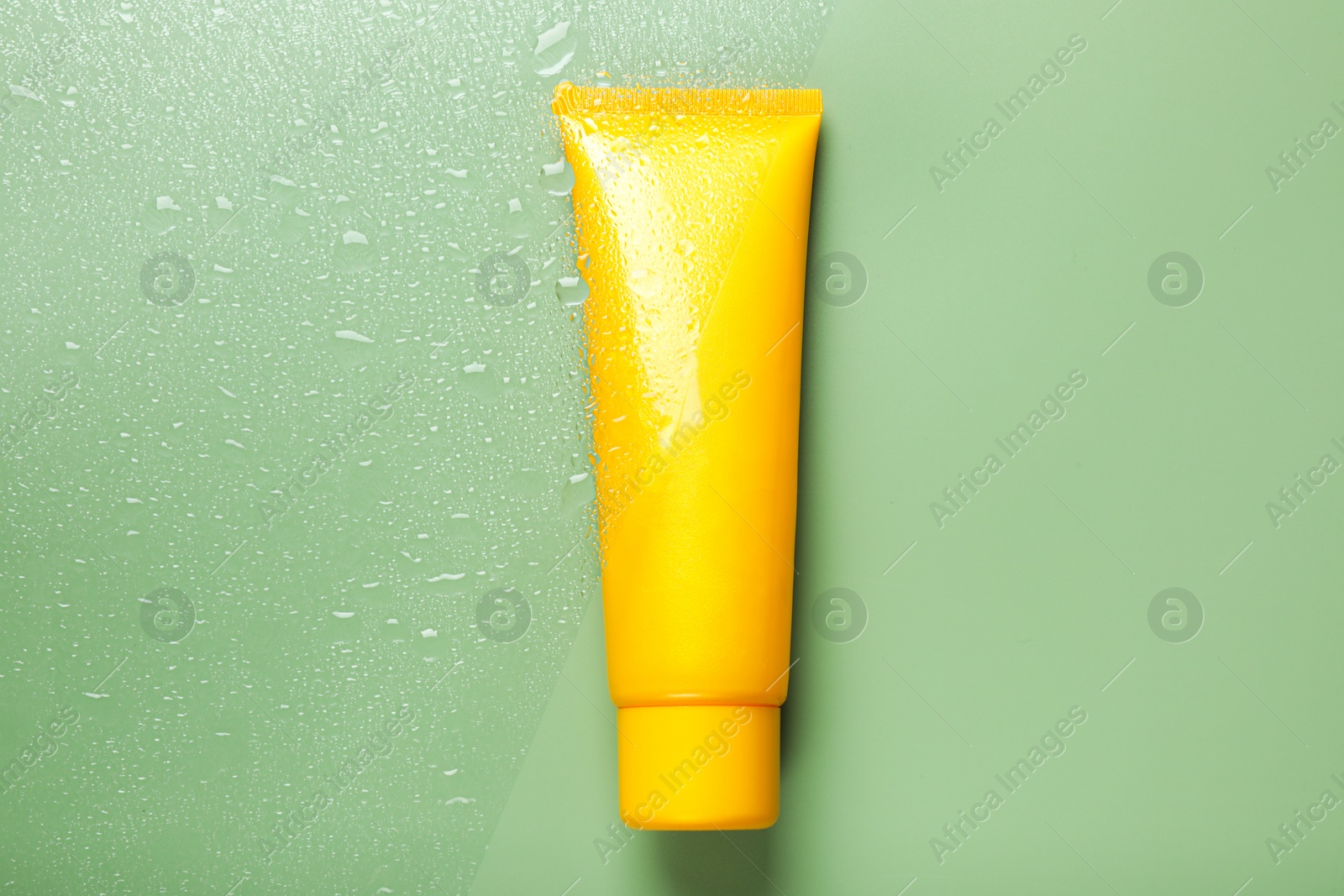 Photo of Tube with moisturizing cream on wet green surface, top view