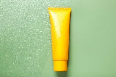 Tube with moisturizing cream on wet green surface, top view