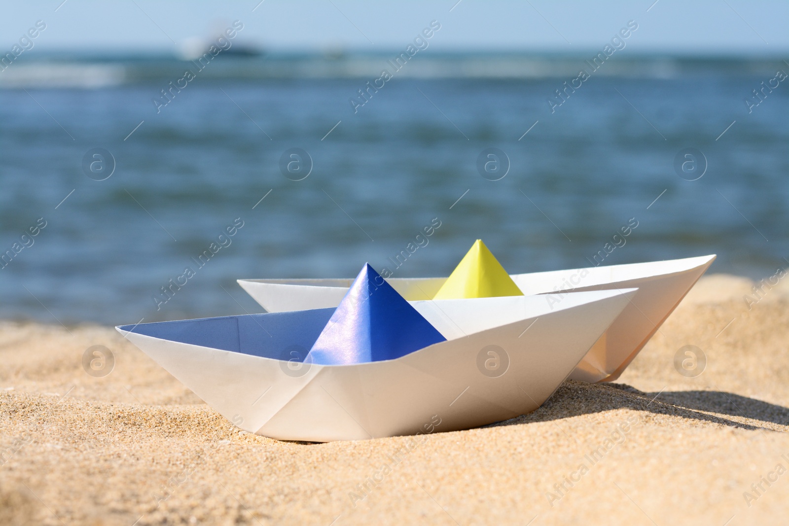 Photo of Two paper boats near sea on sunny day, closeup