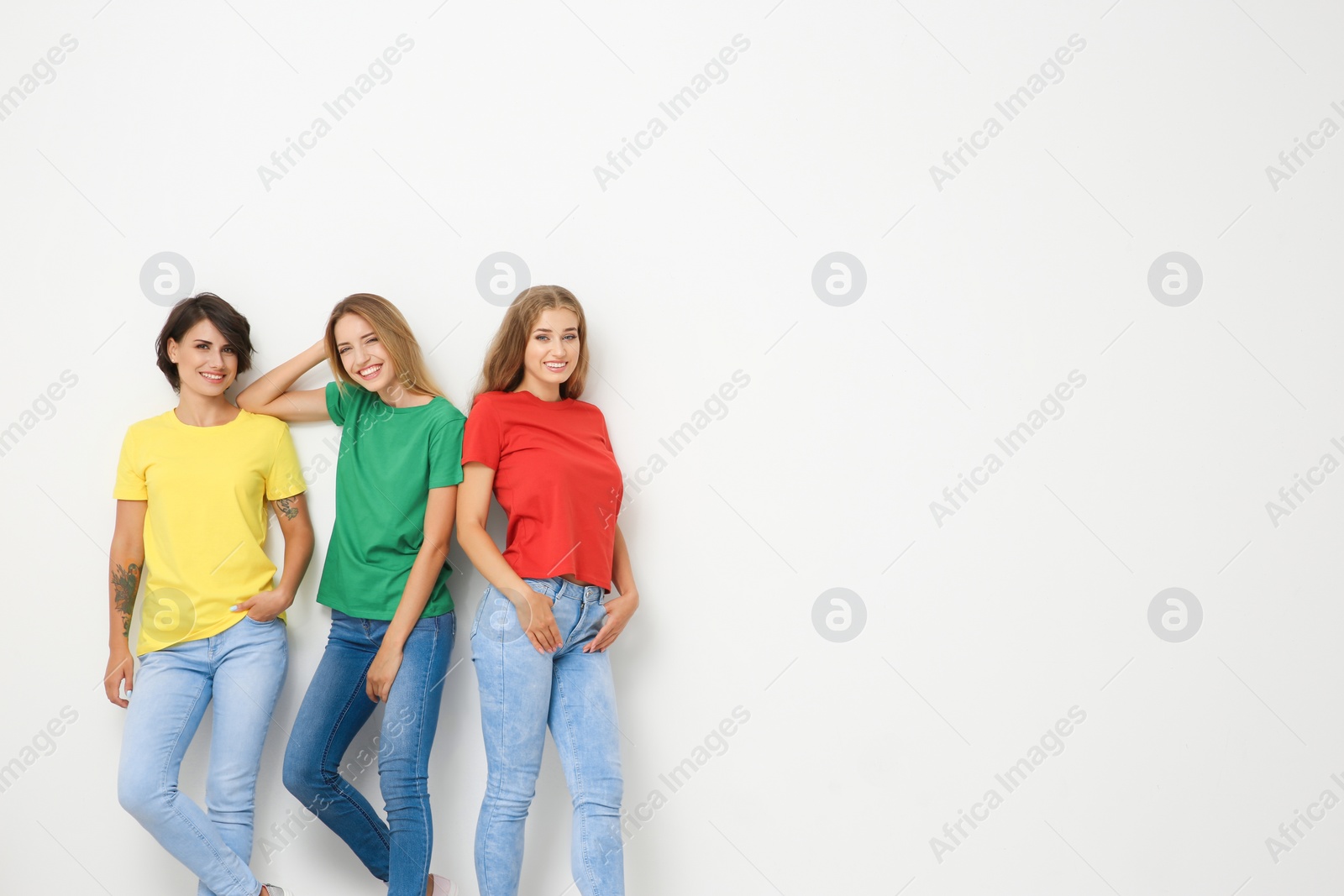 Photo of Group of young women in jeans and colorful t-shirts on light background