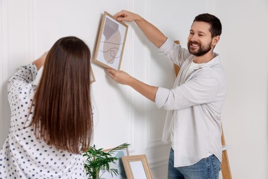Man and woman hanging picture frames on white wall indoors