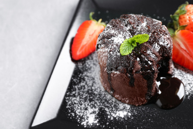 Delicious warm chocolate lava cake with mint and strawberries on plate, closeup