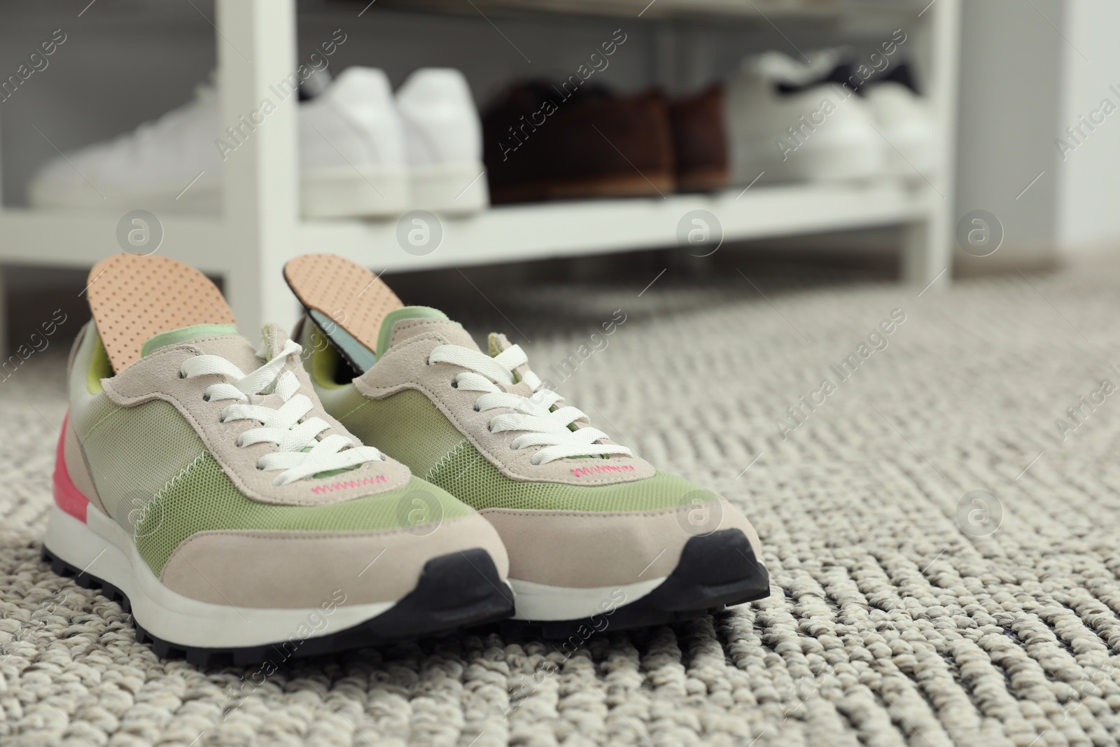 Photo of Orthopedic insoles in shoes on rug, closeup. Space for text