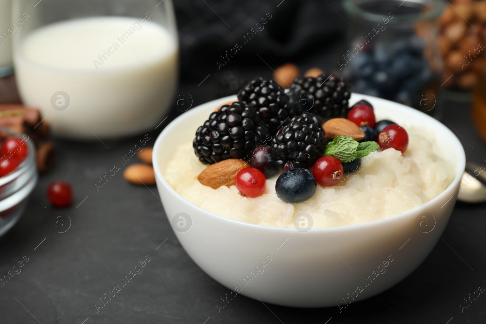 Photo of Delicious rice pudding with berries on black table, closeup